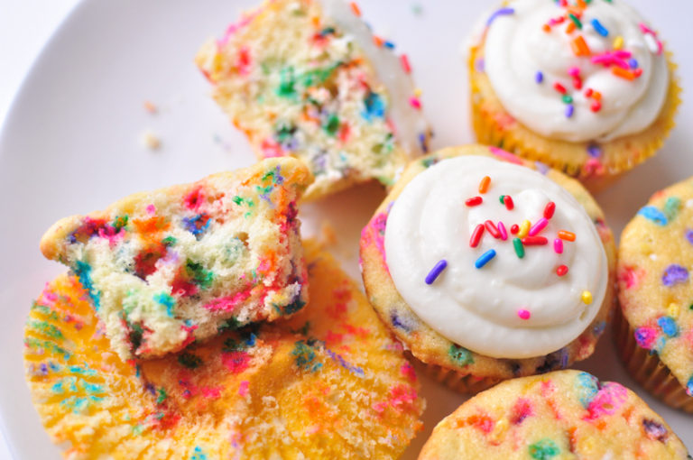 Funfetti Cupcakes on a white plate with one cupcake broken open to see the rainbow sprinkles inside.