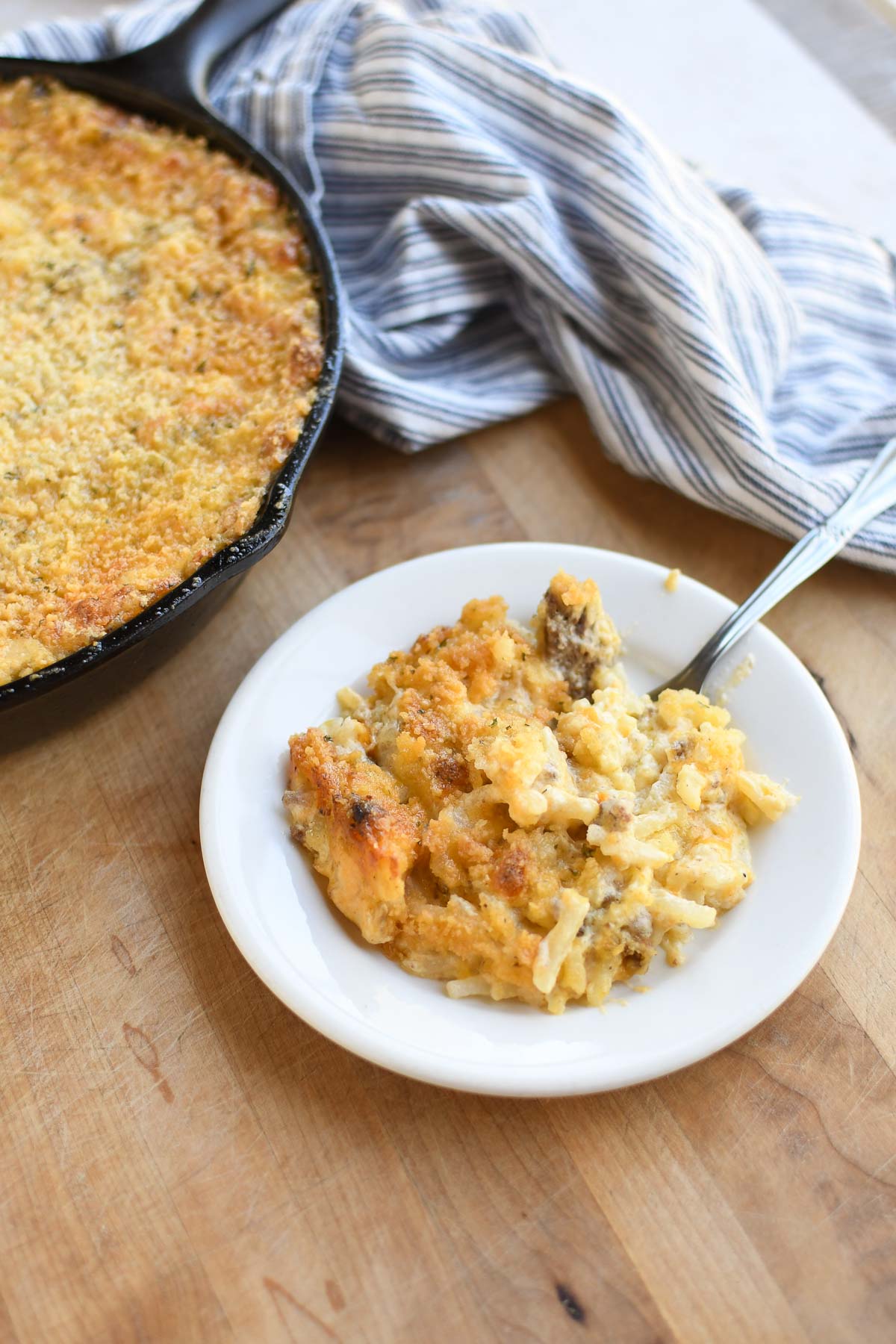 A plate with a serving of hashbrown casserole and a skillet with casserole in the background.