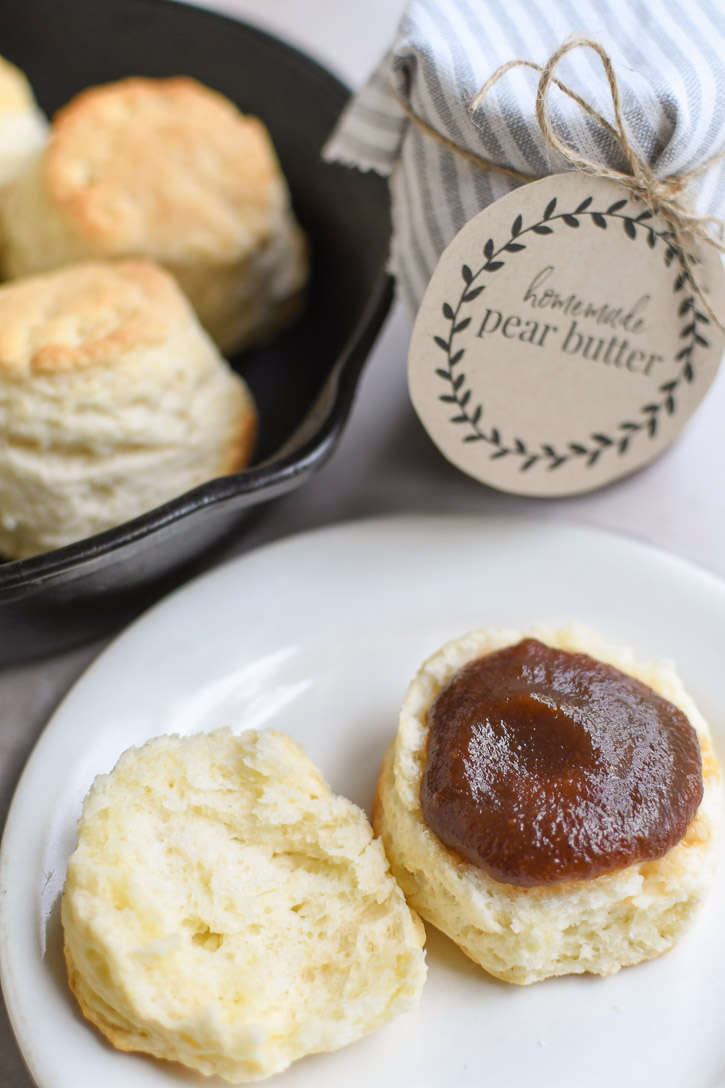 A plate with a biscuit and pear butter with a cast iron skillet in the background