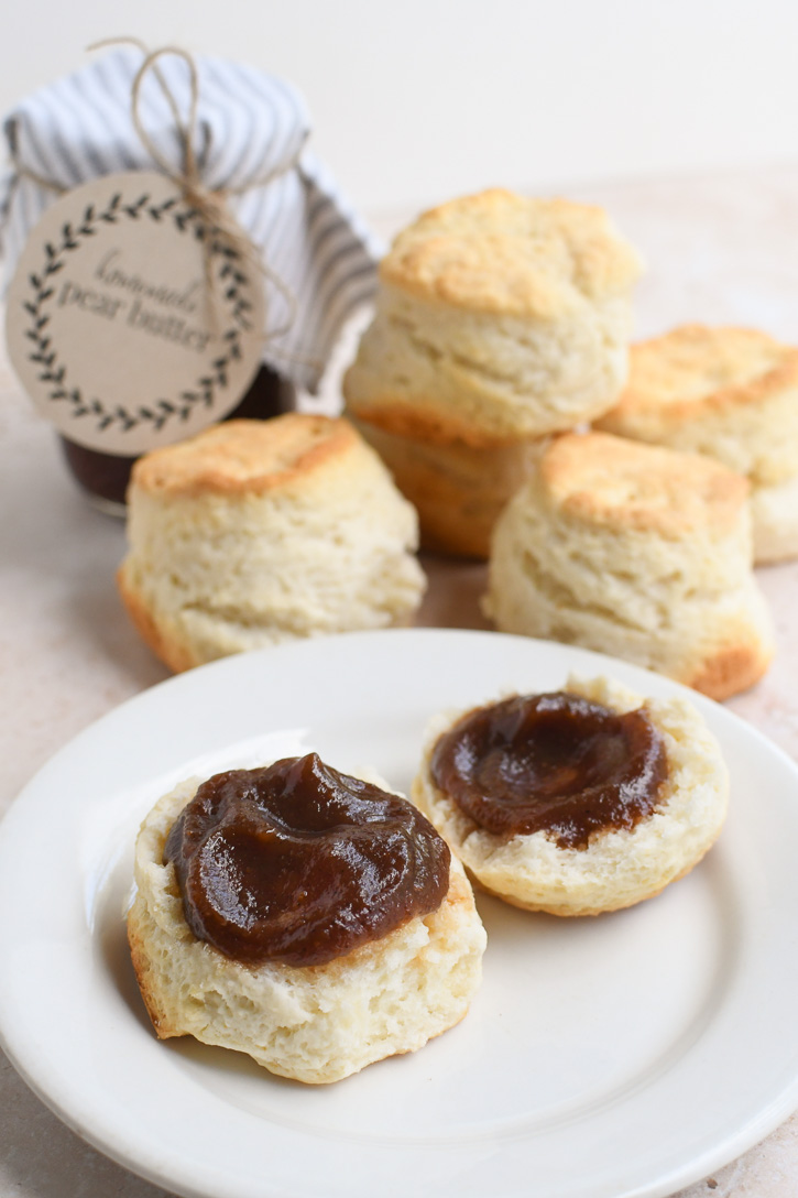 A plate with a biscuit and pear butter and a stack of biscuits