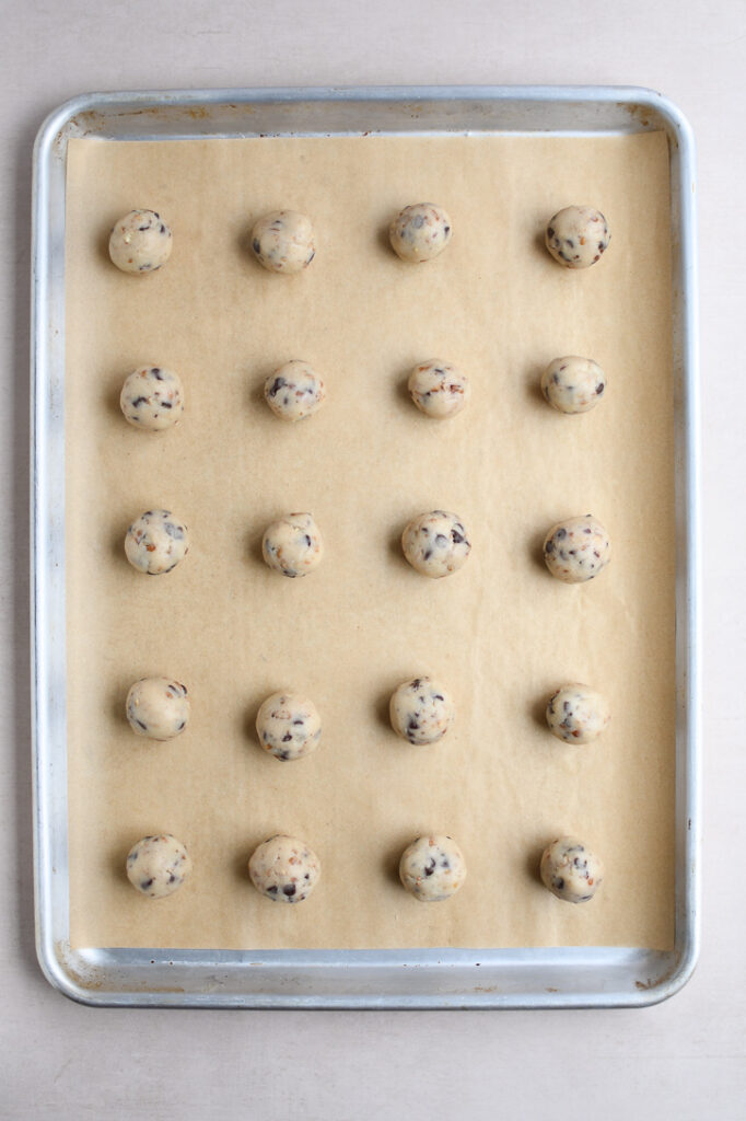 A cookie sheet lined with parchment paper and 20 cookie dough balls rolled and ready to bake