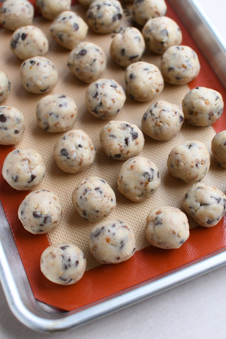 A quarter sheet pan lined with a silicone mat and dozens of snowball cookie dough balls ready to go in the freezer