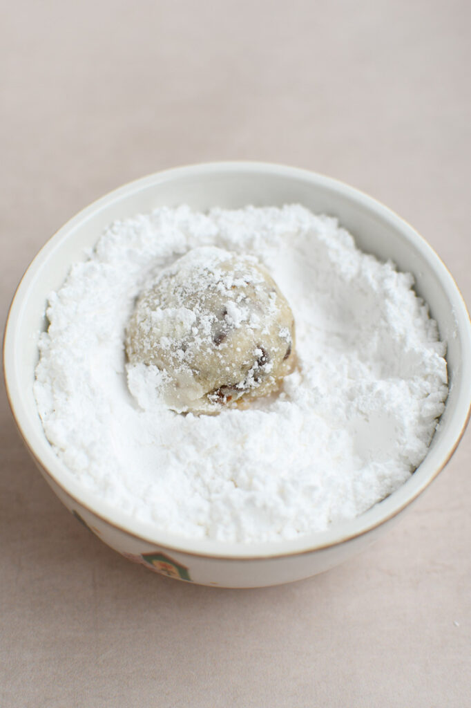 A snowball cookie being rolled in a bowl powdered sugar