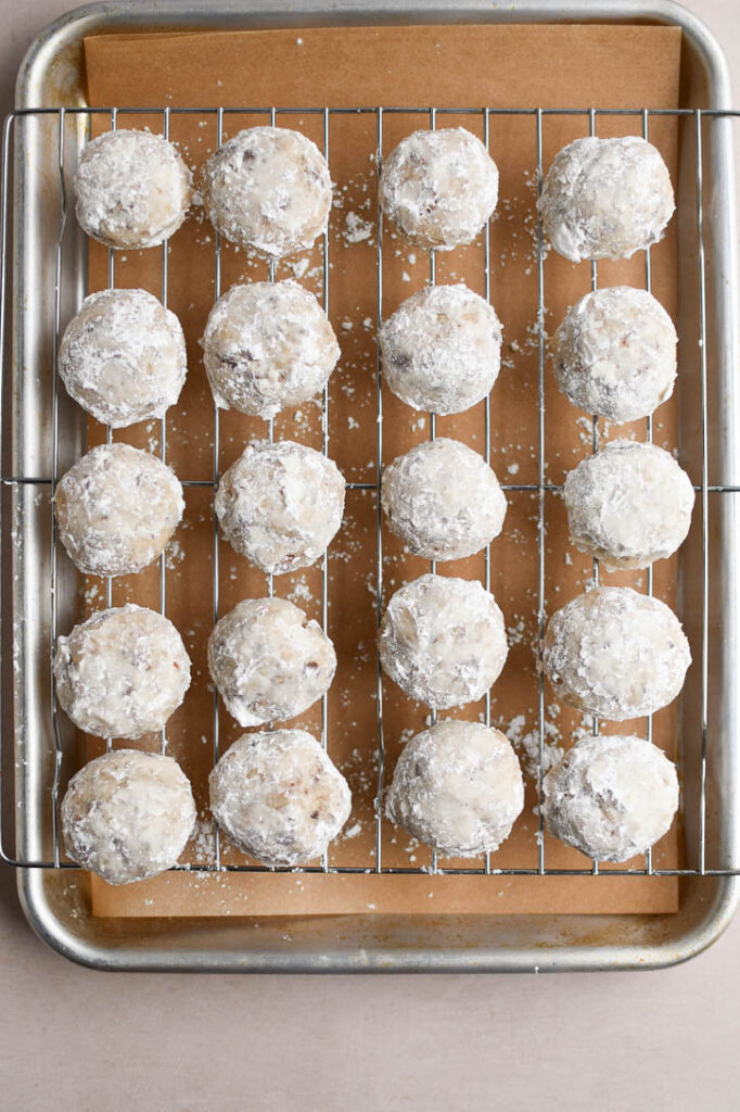 Snowball cookies on a wire rack after the first rolling in powdered sugar 