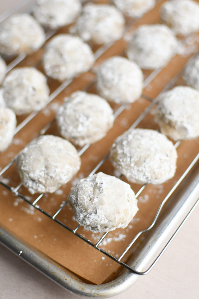 Freshly coated snowball cookies cooling on a wire rack