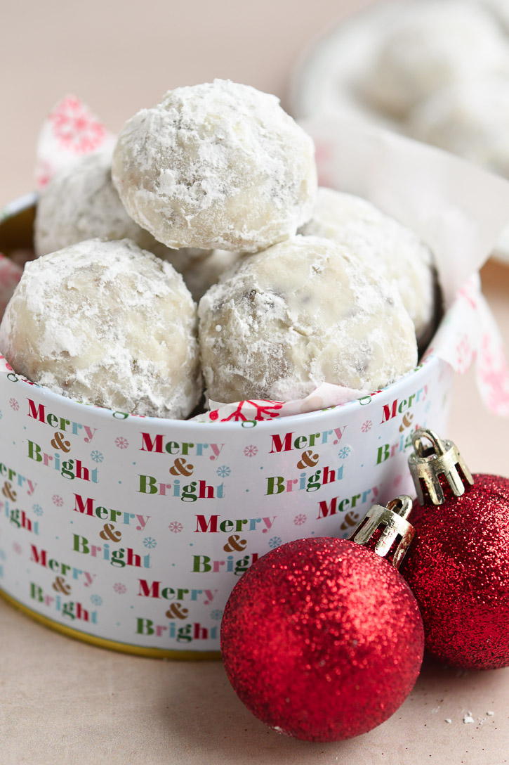 A stack of Snowball Cookies in a Christmas tin