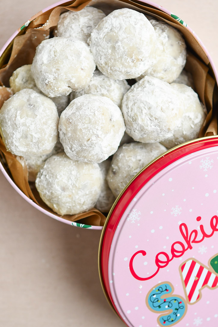 A Christmas cookie tin lined with parchment paper and filled with snowball cookies for gifting