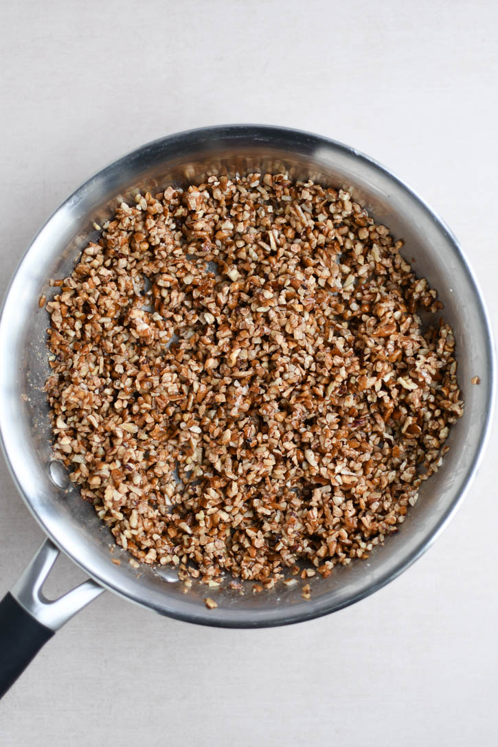 A skillet with buttery toasted chopped pecans