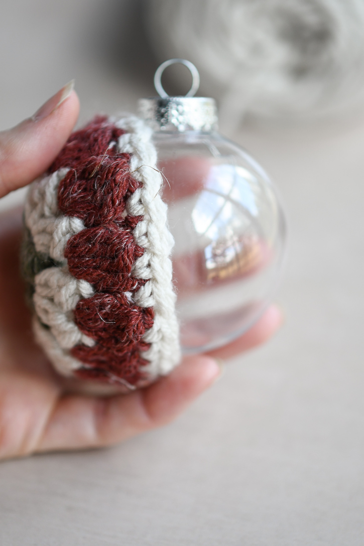 Holding half of the crochet project on the plastic ornament to check the fit