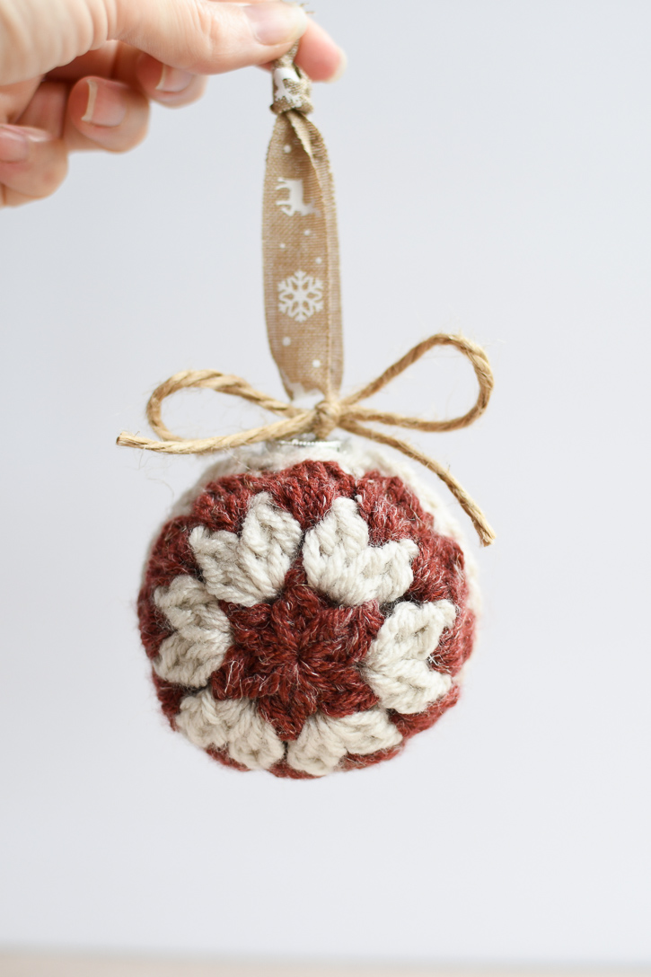 A woman's hand holding a crochet Christmas ornament hanging by a ribbon and tied with a twine bow