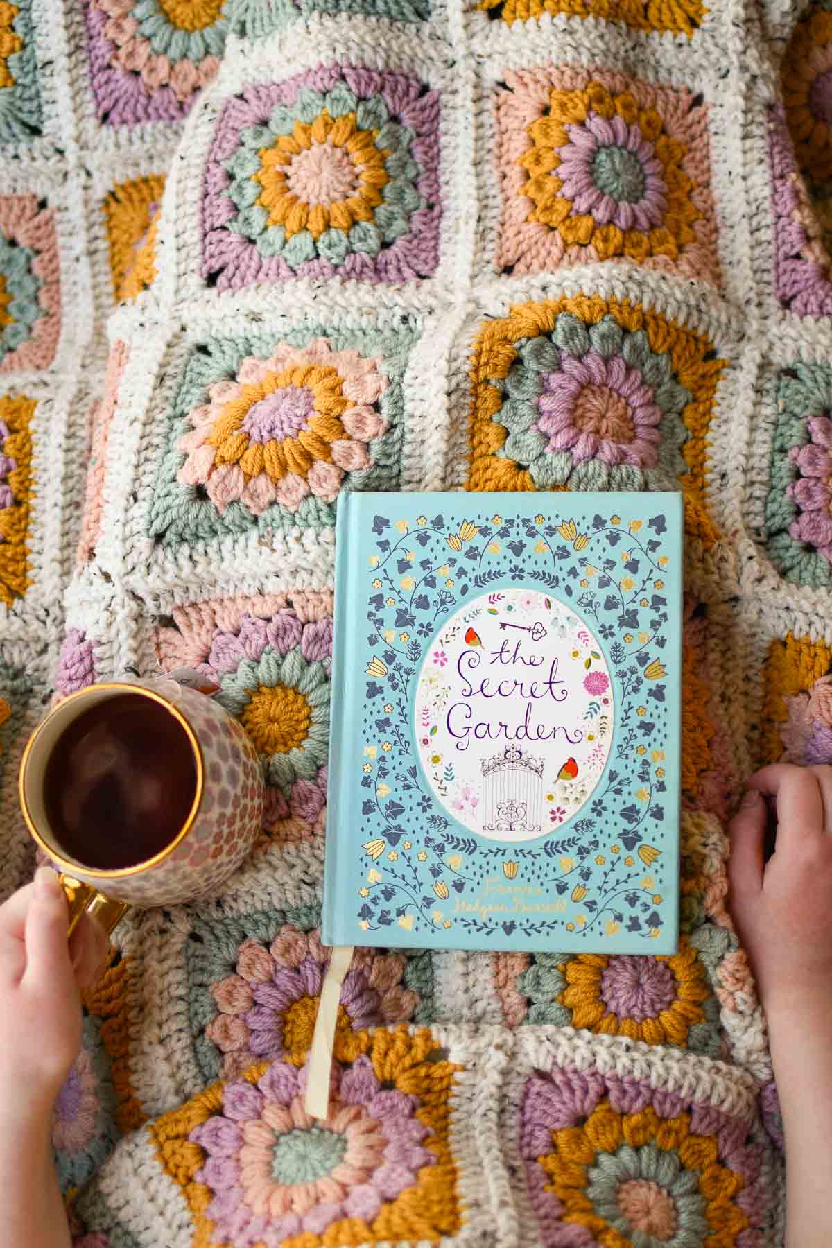 A bright sunburst granny square blanket with a cup of tea and a book