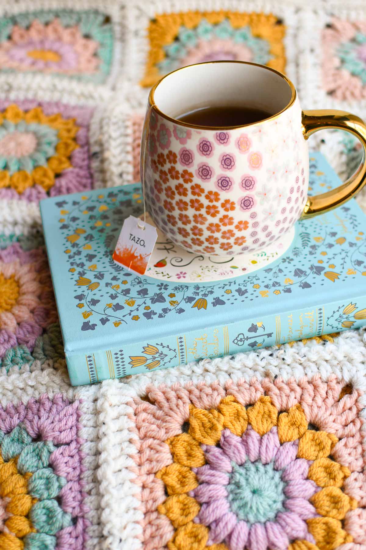 A decorative image showing a finished blanket, with a book, and a cup of tea brewing.